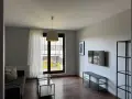 Nowoczesny salon z szarą kanapą, szklanymi stolikami i telewizorem. Widok z okna na zielony dziedziniec, idealne miejsce na relaks w śródmieście Wrocław.