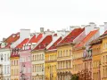Kolorowe kamienice w Warszawie, z czerwonymi dachami i białymi kominami, tworzą malowniczy krajobraz.