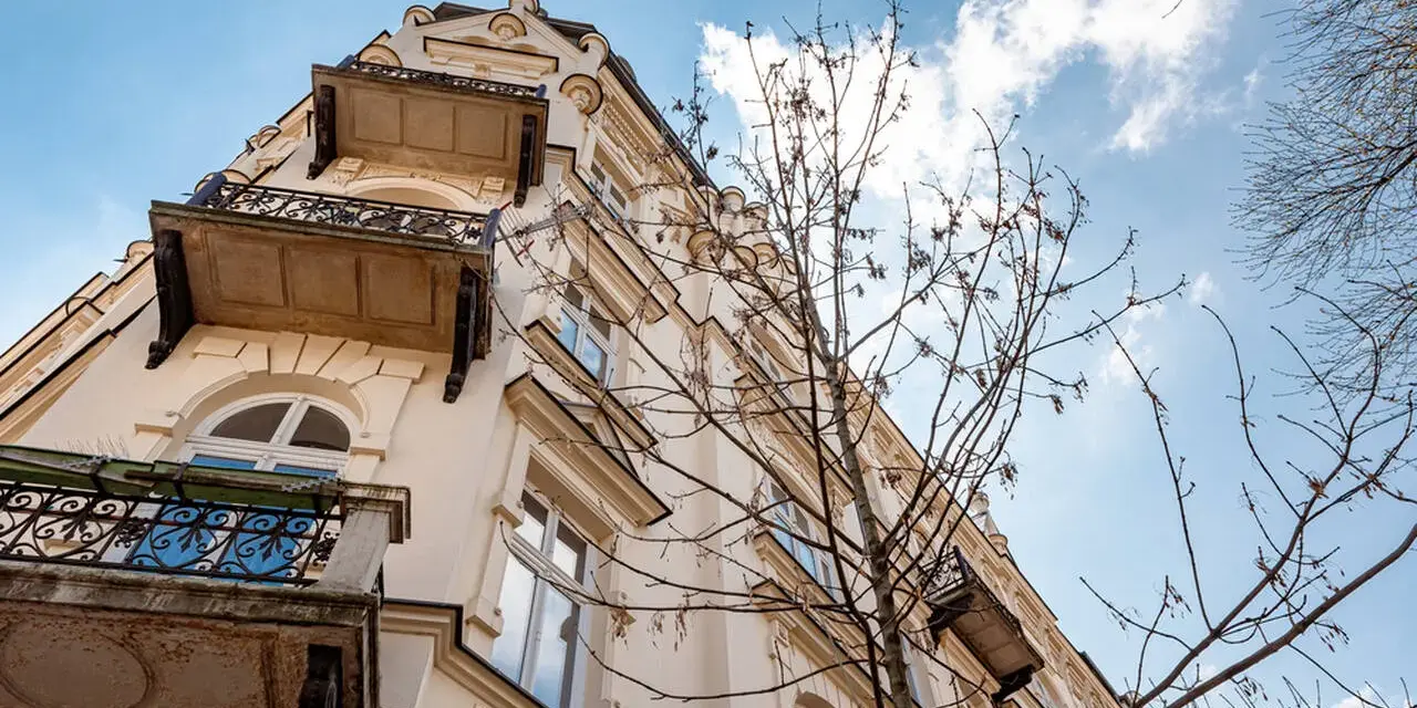Elegancka kamienica z balkonami i ozdobnymi detalami, widziana z dołu na tle błękitnego nieba z chmurami.