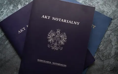 Stos dokumentów, na wierzchu ciemnogranatowy akt notarialny z godłem Polski.