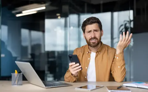 Zdezorientowany mężczyzna trzyma telefon, jakby właśnie dowiedział się o problemach z cesją.