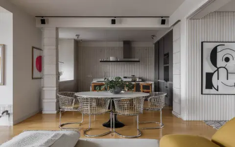 Nowoczesne wnętrze z okrągłym stołem i krzesłami w stylu bauhaus. W tle kuchnia i abstrakcyjne obrazy.