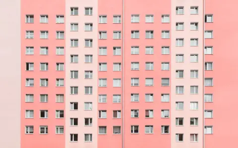 Pasteloza w architekturze: fasada bloku mieszkalnego w odcieniach różu i brzoskwini, z rzędami okien.