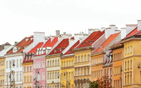 Kolorowe kamienice w Warszawie, z czerwonymi dachami i białymi kominami, tworzą malowniczy krajobraz.