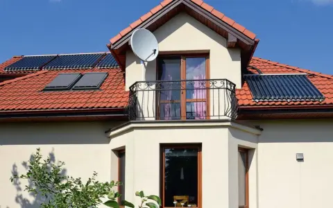 Nowoczesny wykusz w domu z balkonem i oknami, na dachu panele słoneczne i antenę satelitarną.