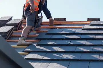 Pracownik w kamizelce odblaskowej układa dachówki, realizując zmianę konstrukcji dachu.